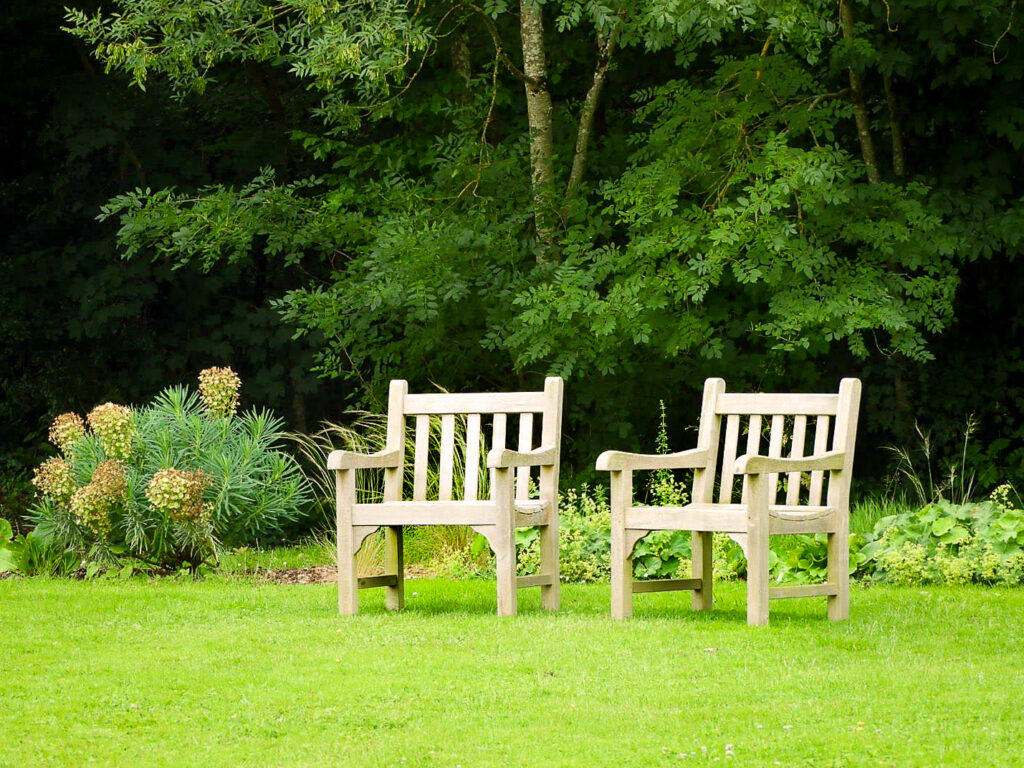 Deux fauteuils de jardin en bois sur une pelouse verte, avec des arbres et des plantes en arrière-plan