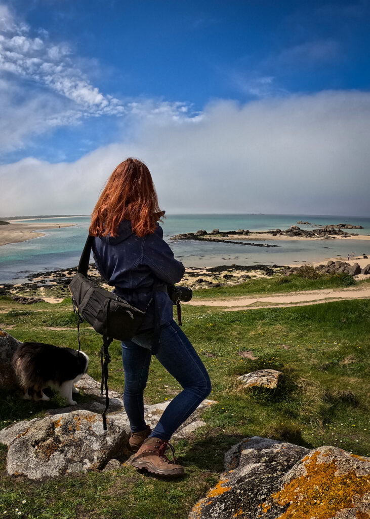 Photographe de dos, observant le littoral breton, équipée d’un sac, accompagnée d’un chien.