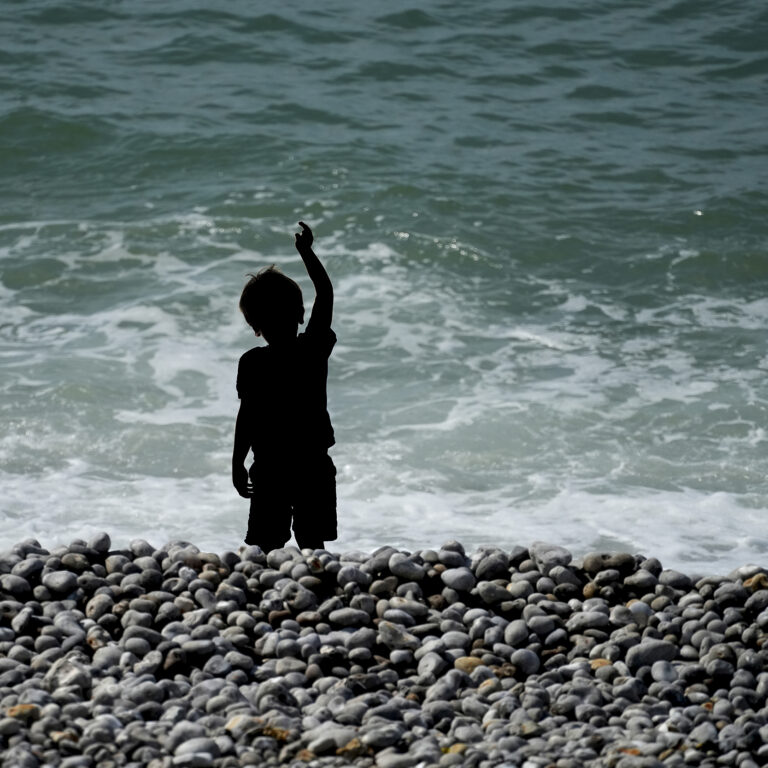 Silhouette d'enfant le bras tendu vers l'invisible face à l'océan - Le bras tendu vers l'invisible, photographie artistique