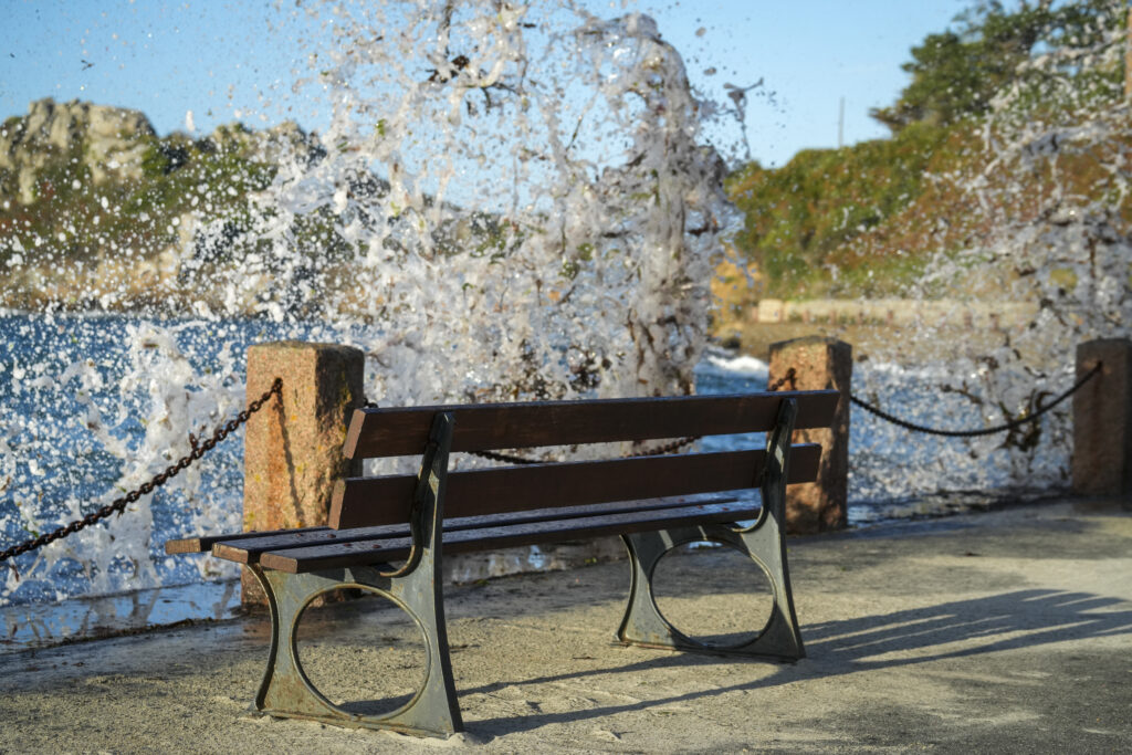 Banc en bois sur un quai, devant des vagues éclatant contre la digue à Trégastel